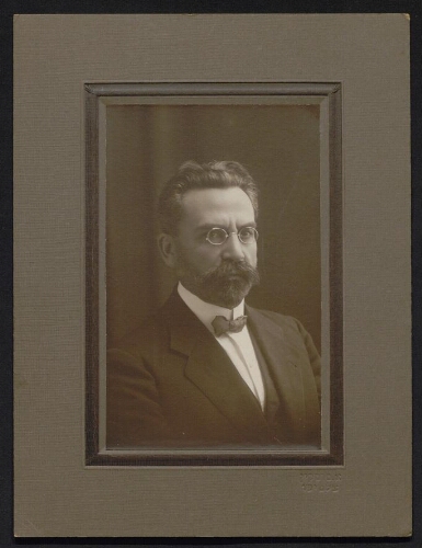 Portrait photographique sur papier cartonné d'un homme portant des lunettes rondes, en costume et nœud papillon, datée du 20 juin 1932