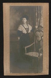 Photographie d'une femme élégante en robe longue, posant à côté d'une chaise vide, datée du 8 novembre 1912