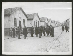 Photographie d'hommes devant des baraques numérotées
