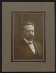 Portrait photographique sur papier cartonné d'un homme portant des lunettes rondes, en costume et nœud papillon, datée du 20 juin 1932