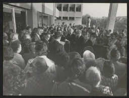 Photographie d'un homme coiffé d'un chapeau noir, prononçant un discours au micro devant une assemblée (Jackie Kennedy parmi eux), non datée