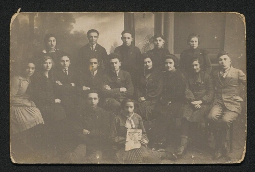 Photographie d'un groupe de jeunes étudiants, jeune fille devant tenant un journal avec nom en yiddish, non datée