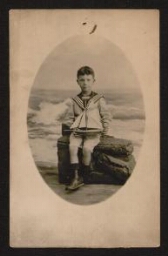 Carte postale d'une photographie d'un jeune garçon en tenue de marin, tenant un petit bateau à voile entre ses mains, datée de juillet 1913