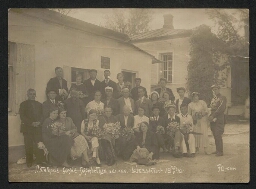 Photographie d'un groupe de personnes posant devant une petite maison et tenant des bouquets de fleurs à la main, datée de l'année 1940